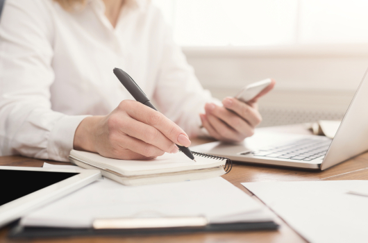 Close up of woman's hands holding smartphone and writing notes in notebook